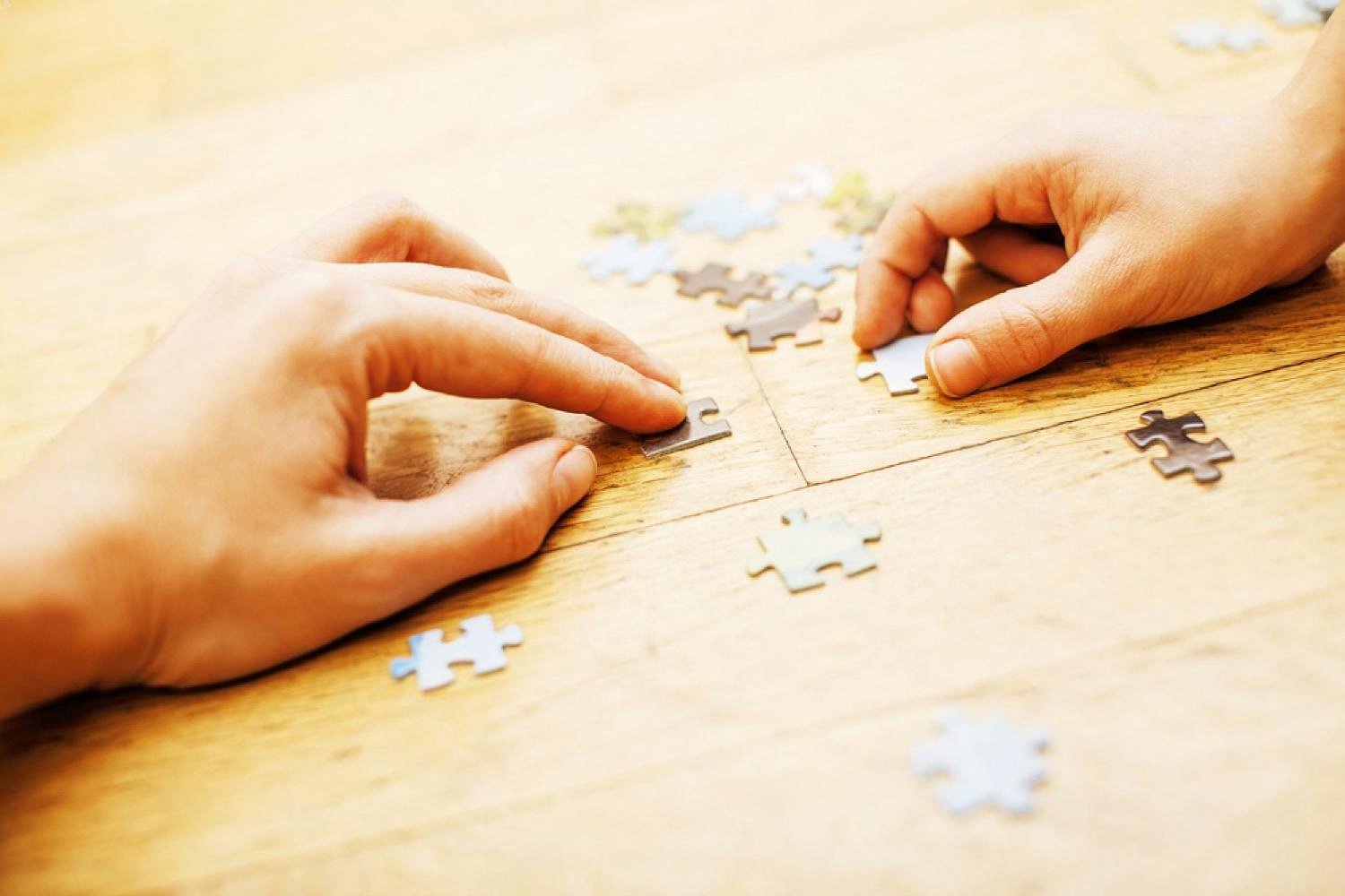 Two hands piecing together a jigsaw puzzle on a warm wooden table